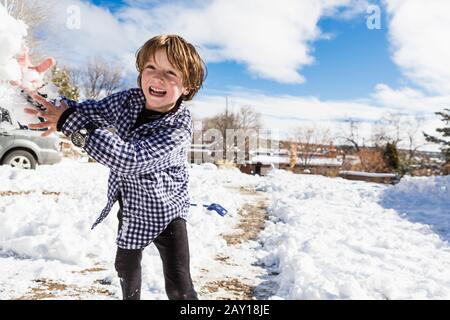 Un garçon de six ans jetant une boule de neige Banque D'Images