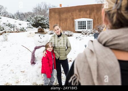 mère prenant portrait de ses enfants avec bonhomme de neige en arrière-plan Banque D'Images