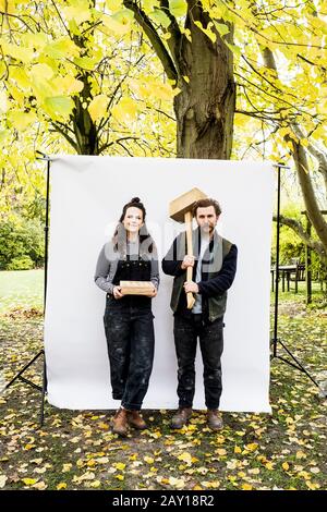 Portrait d'une femme et d'un homme barbu tenant des blocs de bois debout devant un fond blanc dans un jardin, regardant l'appareil photo. Banque D'Images