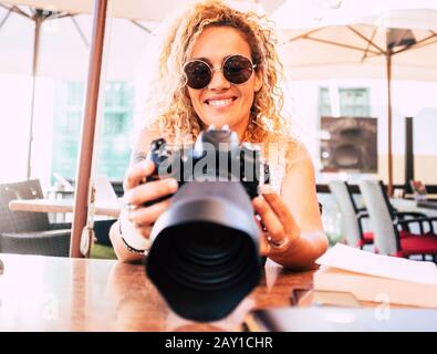 Gai belle femme avec un grand appareil photo reflex professionnel moderne regardant les images dans l'arrière écran souriant - les gens avec la technologie et Banque D'Images