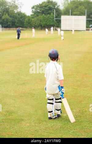 Match de cricket, vue arrière d'un jeune garçon tenant une batte de cricket en attente de jouer.