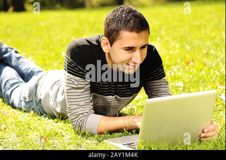Un jeune homme heureux qui s'est posé sur l'herbe verte dans la nature et travaille sur un ordinateur portable Banque D'Images