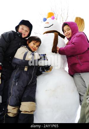 Les enfants jouent avec joie dans la neige en faisant du bonhomme de neige, saison d'hiver Banque D'Images