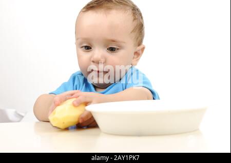 Mignon adorable bébé d'un an avec des yeux verts mangeant sur la table, la cuillère et la plaque Banque D'Images