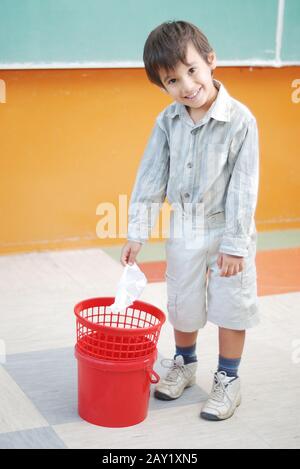 Peu cute boy throwing paper dans la corbeille Banque D'Images