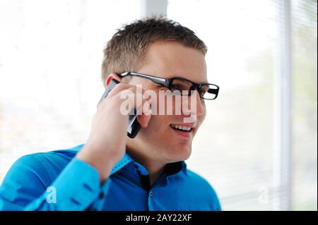 Portrait d'un jeune homme heureux parlant sur le téléphone mobile tout en regardant par la fenêtre Banque D'Images