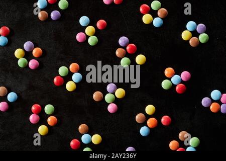 Groupes colorés de cinq bonbons enrobés de sucre formant un motif aléatoire dispersé sur fond noir en plein cadre Banque D'Images