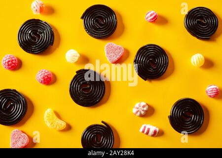 Spirales de réglisse avec des bonbons fruités de jub entre dispersés sur un fond jaune dans un motif décoratif de la tête Banque D'Images