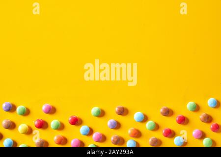 Bordure colorée en bonbons avec bonbons enrobés de sucre dans des couleurs arc-en-ciel parsemées d'un fond jaune vif avec espace de copie Banque D'Images