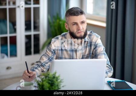 Jeune homme aux cheveux sombres qui travaille derrière un ordinateur portable blanc. Banque D'Images