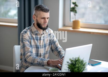 Jeune homme travaillant derrière un netbook blanc. Banque D'Images
