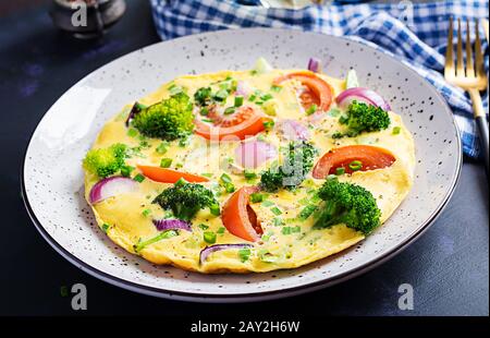 Omelette avec brocoli, tomates et oignons rouges sur la table sombre. Frittata italienne avec légumes. Banque D'Images