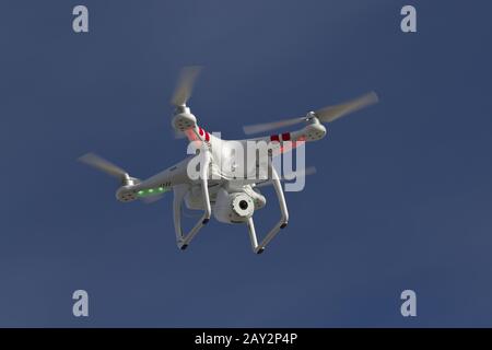 Petit hélicoptère sans pilote avec un appareil photo flottant dans le ciel bleu Banque D'Images