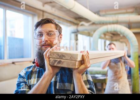 Les apprentis charpentiers portent des poutres en bois dans l'atelier de menuiserie Banque D'Images