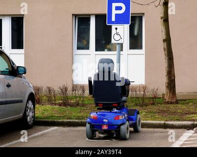 scooter électrique bleu à handicap motorisé ou scooter à handicap dans le stationnement pour handicap. panneau bleu et blanc sur le poteau en aluminium. symbole de stationnement. Banque D'Images