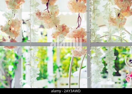 Belles fleurs artificielles accrochées sur des fenêtres en verre pour décorer pour une fête de jardin. Vue depuis la fenêtre sur la vitre. Banque D'Images