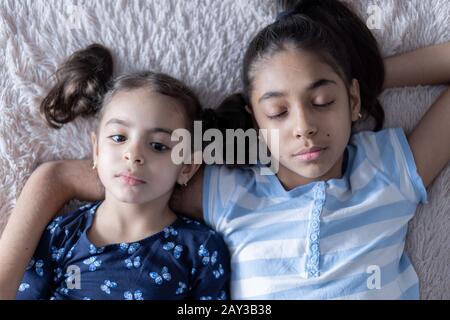 Deux jeunes filles mignons du Moyen-Orient, sœurs, se trouvent sur le lit et regardent le smartphone dans les rayons du soleil. Des filles persanes sur le lit avec un téléphone Banque D'Images