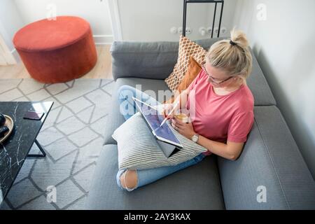 Woman on sofa using digital tablet Banque D'Images