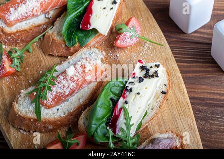 Sandwichs au poisson rouge, au bœuf en suvit et au fromage doux. Garnies de tranches de microvert, d'arugula et de tomates. Sur un plateau ovale en bois espace de copie Banque D'Images