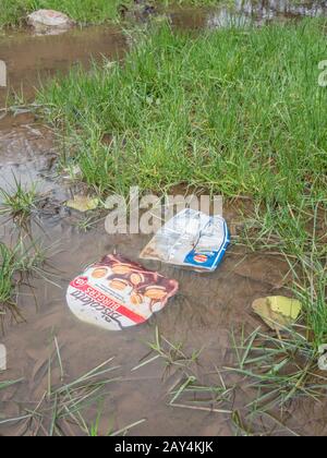Vider l'emballage alimentaire en plastique flottant dans la flaque d'eau après de fortes pluies d'hiver. La guerre de métaphore sur le plastique souple, la litière en plastique, l'emballage alimentaire problématique. Banque D'Images