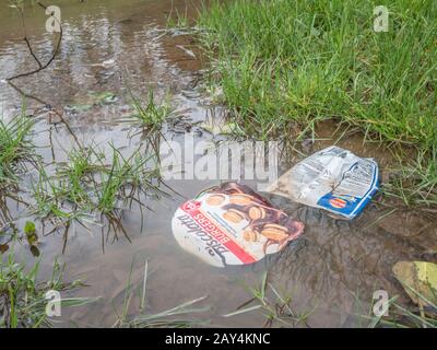 Vider l'emballage alimentaire en plastique flottant dans la flaque d'eau après de fortes pluies d'hiver. Guerre métaphore sur plastique, litière plastique, emballage alimentaire problématique. Banque D'Images