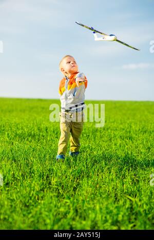 Happy boy playing with toy airplane contre le ciel d'été bleu et vert en arrière-plan sur le terrain. Banque D'Images