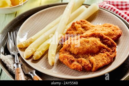 Apéritif gastronomique avec pointes d'asperges blanches servies avec du poisson doré frit ou du schnitzel sur une plaque rustique en gros plan avec des ustensiles adaptés à la Banque D'Images