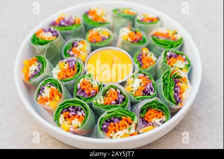 Concept de nourriture végétalienne. Délicieux rouleaux de printemps verts en papier de riz et épinards, remplis de légumes frais hachés. Petite assiette avec sauce curry jaune Banque D'Images