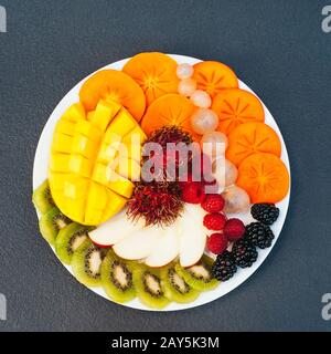 Tranches de fruits exotiques mûrs sur plaque blanche. Kiwi, mangue, framboise, myrtille et persimmon. Assortiment de fruits. Vue de dessus. Concept de régime alimentaire sain Banque D'Images