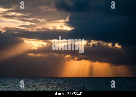 Les rayons de soleil orange éclatent dans les nuages au-dessus de la mer calme des caraïbes pendant le coucher du soleil. Banque D'Images