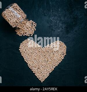 Garbanzo ou pois chiches séchés sains déversés à partir de bocal en verre, haricots crus organiques en forme de coeur isolés sur fond noir. Cuisine vivante et bien-être Banque D'Images