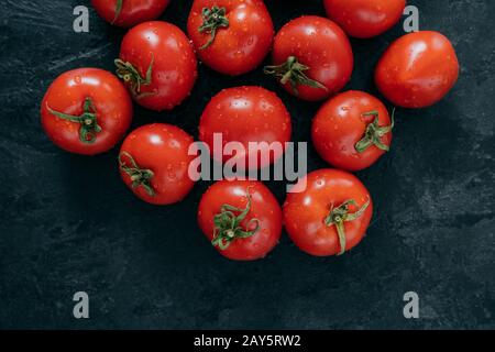 Tomates rouges fraîchement récoltées avec des feuilles vertes sur fond sombre. Aliments naturels naturels biologiques sains. Tomates crues juteux. Légumes frais Banque D'Images