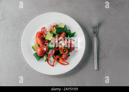 Vue de dessus de la salade de légumes frais préparée de poivron rouge, de radis, de tomates, de concombres et de persil dans un bol blanc, fourche près. Concept de plats végétariens. H Banque D'Images