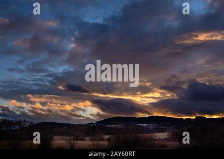 Beau coucher de soleil - ciel rouge sur paysage vallonné, ciel bleu avec nuages de couleur orange Banque D'Images