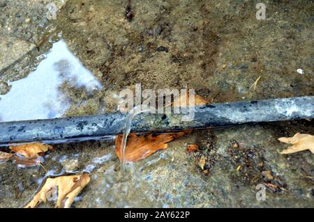 Tuyau d'eau en plastique sur le sol avec une fuite d'eau. Banque D'Images