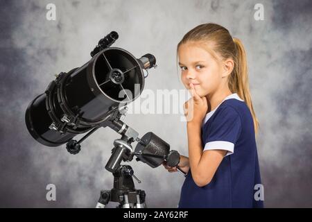 Fille de sept ans pensivement cherche dans la photo, debout au télescope Banque D'Images