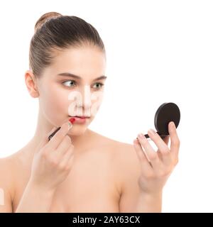 Jeune femme brune avec un visage propre appliquer le rouge à lèvres à l'aide d'un miroir. Isolé sur fond blanc. Banque D'Images