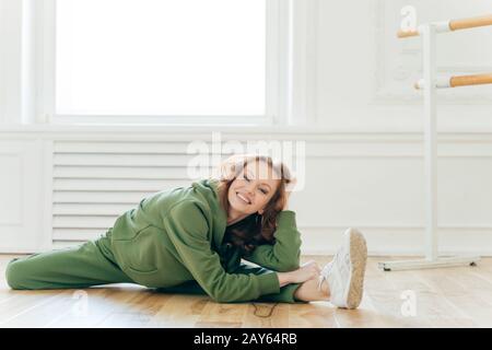 La jeune femme caucasienne aux cheveux rouges montre une bonne flexibilité, fait la coupe des jambes, se prépare à la répétition du ballet, pratique le ballet au studio de danse Banque D'Images