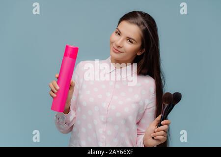 La femme brunette à poil long satisfait utilise un spray pour faire des cheveux élégants, des brosses cosmétiques pour appliquer de la poudre sur le visage, prépare pour occ spécial Banque D'Images