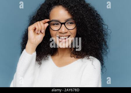 Gros plan de la gaie femme porte des lunettes, garde la main sur le cadre, semble gladeusement de côté, note quelque chose d'impressionnant dans la distance, vêtu d'une wh décontractée Banque D'Images