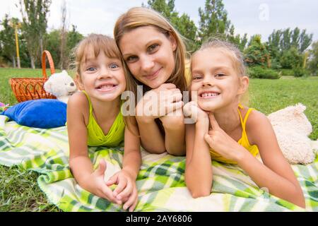 La mère et les deux filles couché dans l'herbe sur un pique-nique et un regard amusant sur le châssis Banque D'Images