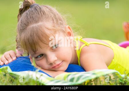 Fille de cinq ans se trouve sur un lit sur un pré vert et bien regarde de côté Banque D'Images