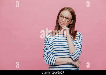 Studio tourné d'une jolie femme avec des cheveux bruns, traverse la main sur la poitrine, garde la main sous le menton, focalisé avec l'expression pensive de côté, porte translat Banque D'Images