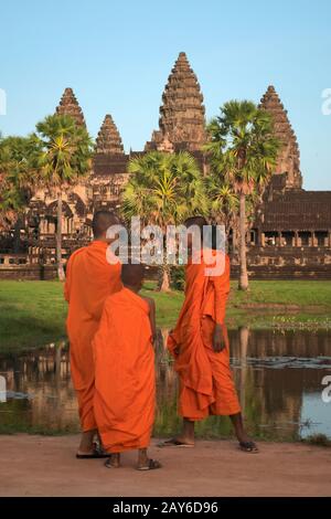 Trois jeunes moines bouddhistes à Angkor Wat, au Cambodge, dans des robes de safran traditionnelles, contemplant le majestueux temple. Banque D'Images