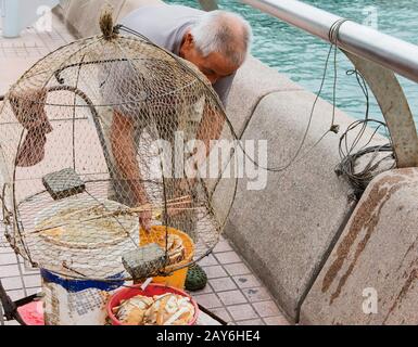 Vieux pêcheur chinois avec son filet de pêche au port de Victoria de HongKong Banque D'Images