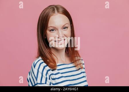 Tourné vers le côté agréable de plaisir à la femme brune avec les cheveux raides, la peau saine, agréable sourire, habillé en pull rayé décontracté, isolat Banque D'Images