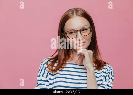 Photo d'une belle jeune femme est titulaire d'chin, porte des lunettes, des vêtements décontractés, envisage de quelque chose, les modèles sur fond rose wit Banque D'Images