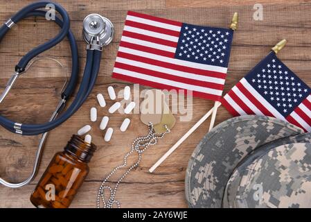 Concept De Soins De Santé Militaires. Chapeau de camouflage, étiquettes de chien, stéthoscope, pilules, et drapeaux américains sur un fond de bois. Banque D'Images