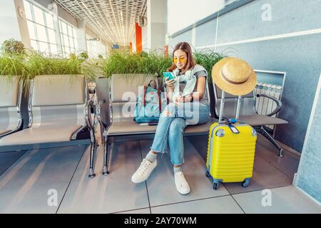 Jeune femme asiatique passager fuyant smartphone en attendant et assis dans le terminal de l'aéroport ou de la gare Banque D'Images