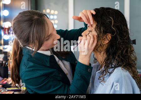 Professionnel maquillage artiste faire le maquillage à une belle jeune fille dans l'étude mignonne Banque D'Images